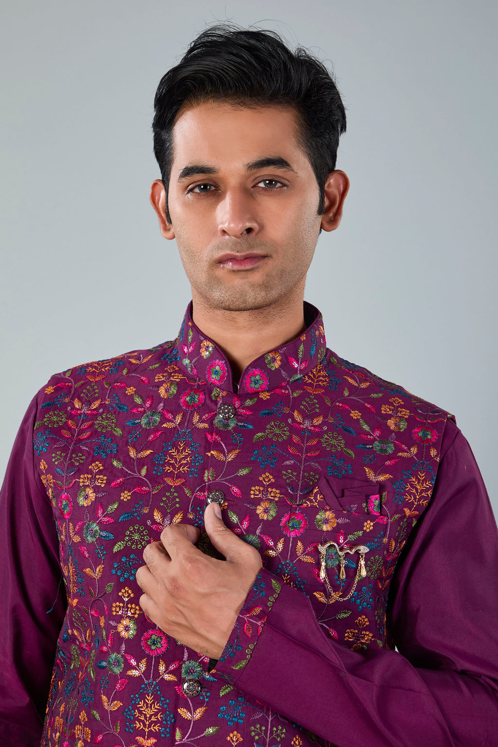 Man wearing a purple traditional outfit with a floral pattern on a gray background