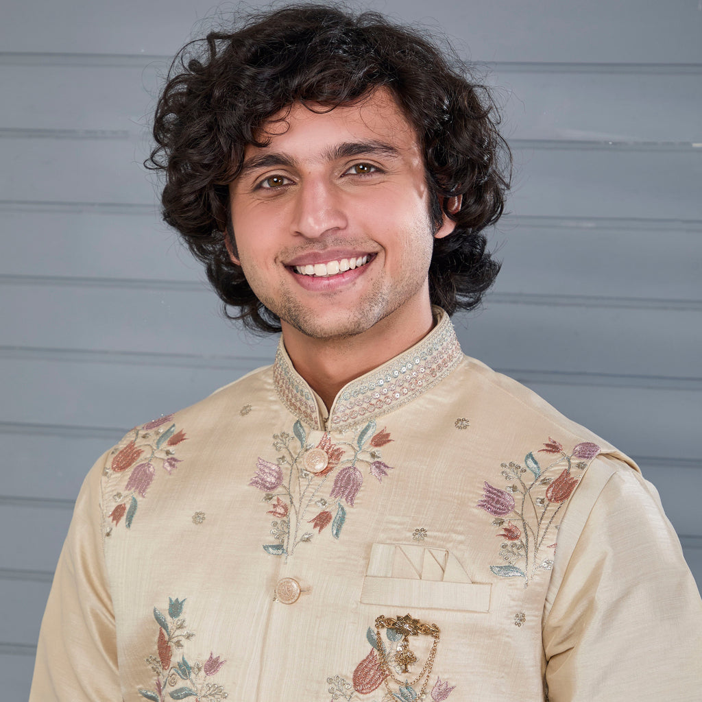 Man wearing a beige embroidered traditional outfit against a gray background