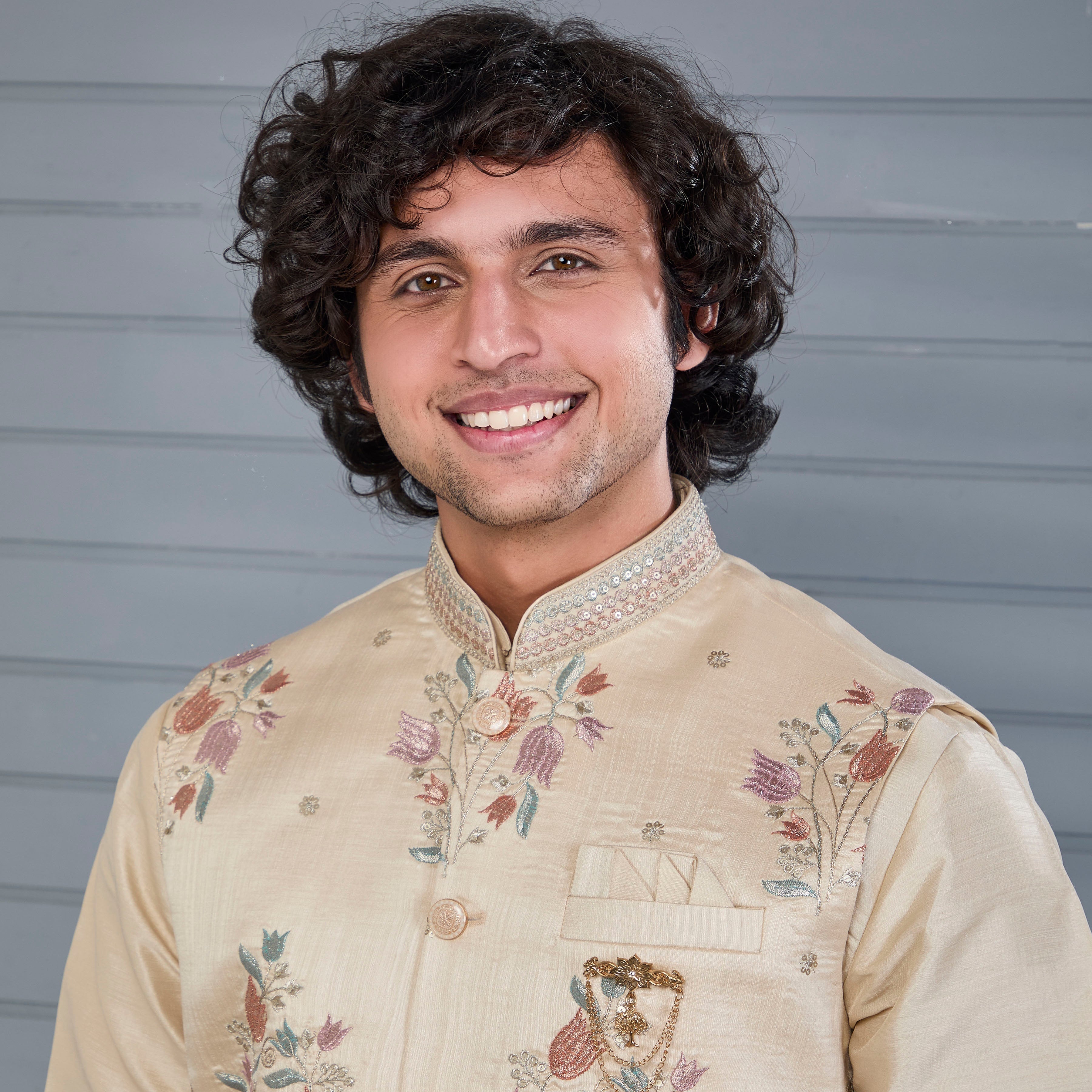 Man wearing a beige embroidered traditional outfit against a gray background