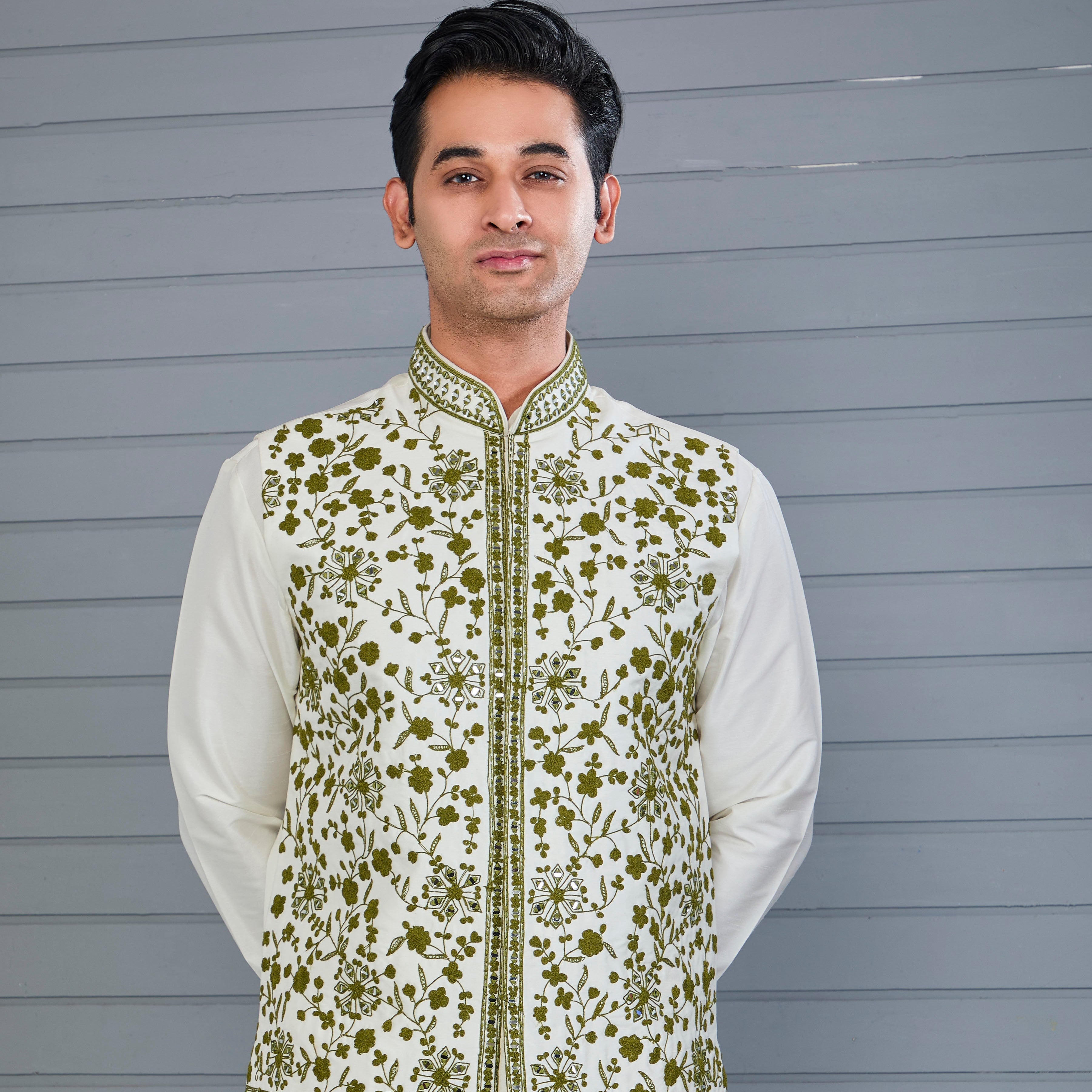 Man wearing a traditional outfit with a floral embroidered vest against a gray background